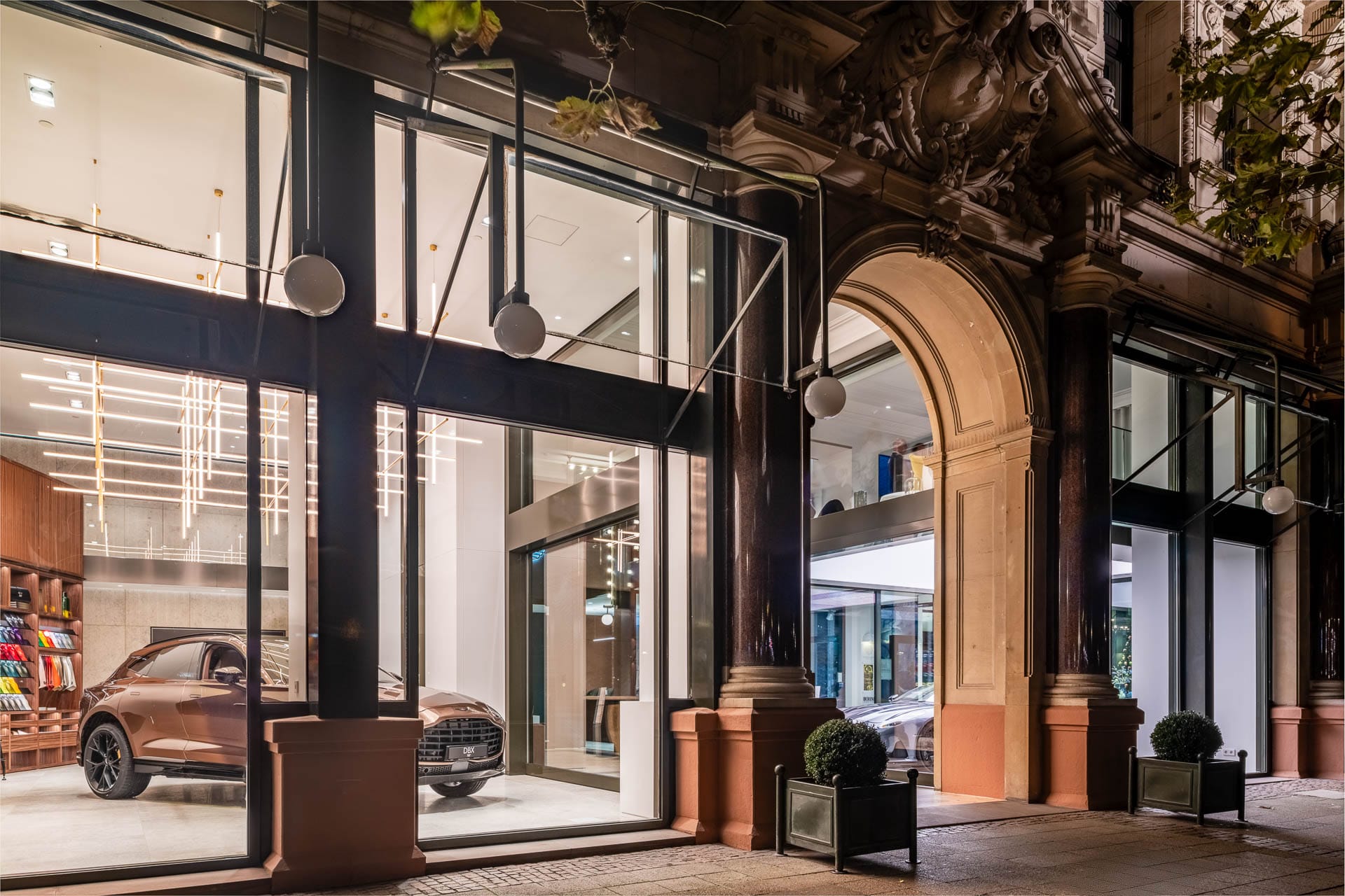 Aston Martin Showroom im historischen Goldenen Kreuz in Baden-Baden bei Nacht, mit beleuchtetem Schaufenster und edlem Fahrzeug im Inneren.