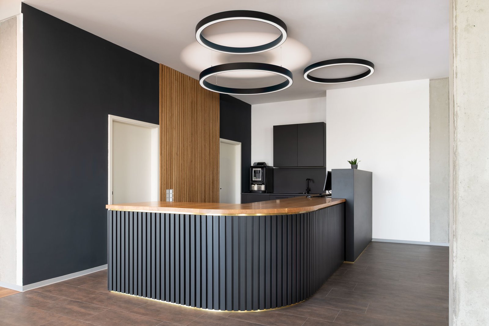 Moderne Rezeption mit geschwungener Holztheke und kreisförmigen Deckenleuchten im Fitnessstudio „Adam & Eve“ in Baden-Baden.