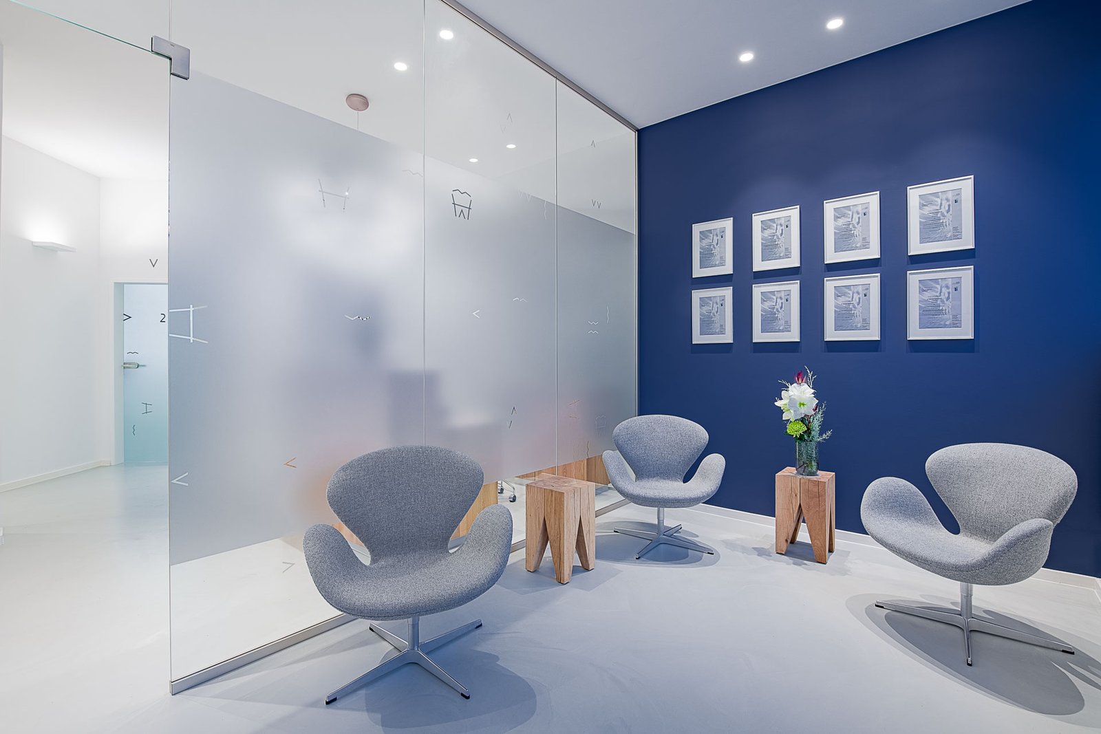 Modernes Wartezimmer mit blauer Akzentwand, Designstühlen und Glasabtrennung in einer Zahnarztpraxis